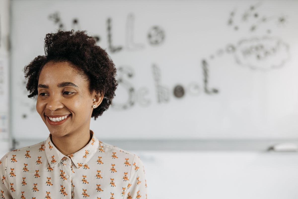 A teacher smiling beside a classroom whiteboard